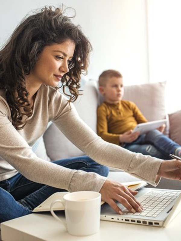Woman sitting on her couch next to her son working at her laptop